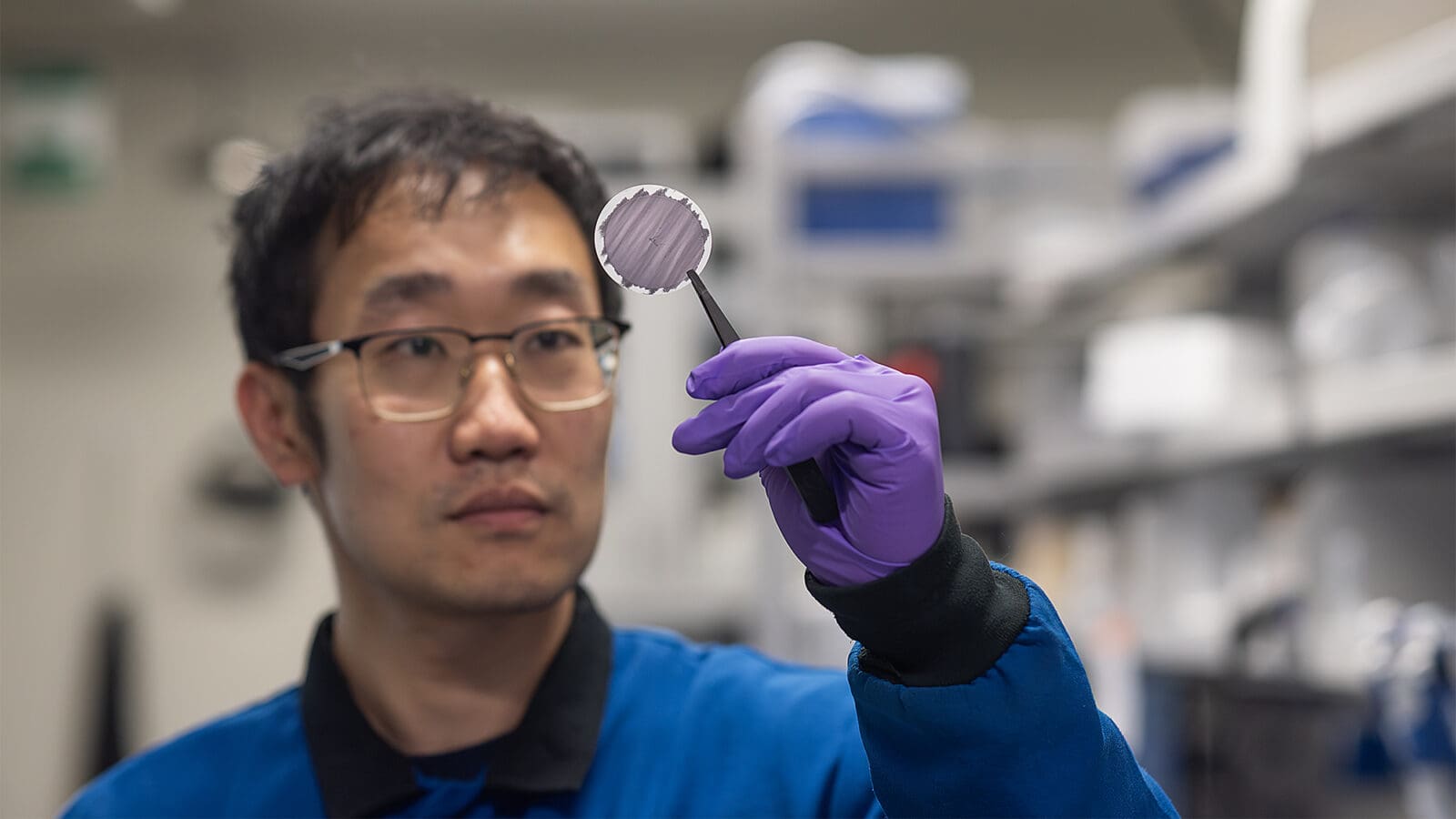 A researcher holds up a circular disc with tweezers