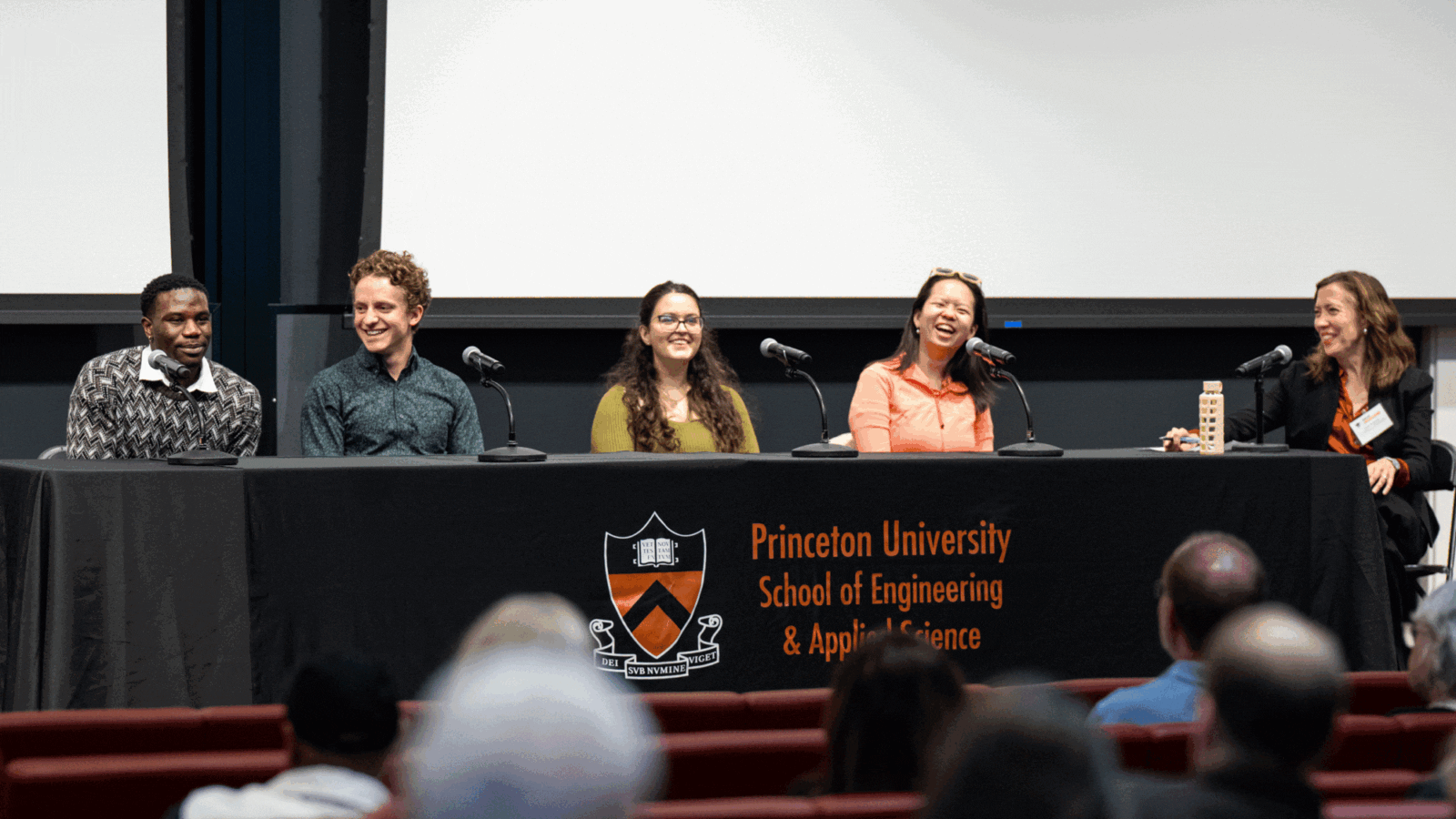 Five panelists share a laugh onstage before an audience