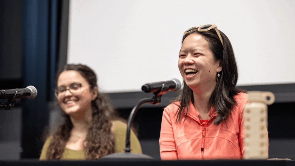 Two women sitting at microphones before a large movie screen.