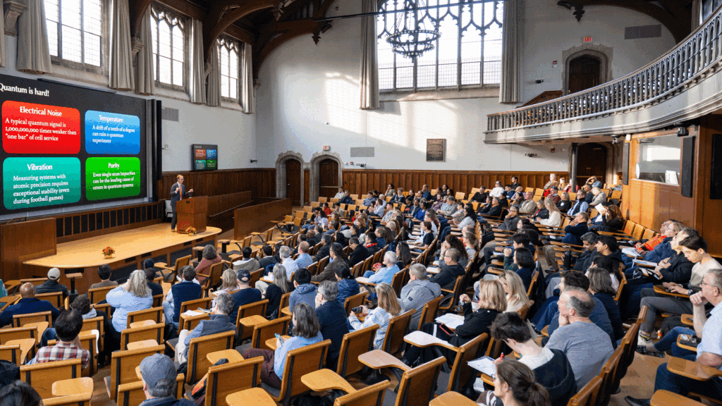 a speaker at a podium before a crowd seated in an auditorium.