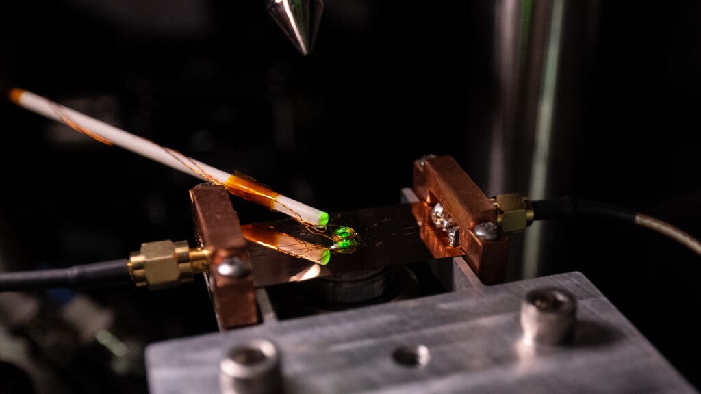 Experimental setup with green laser light and a small diamond sample between metal contacts.