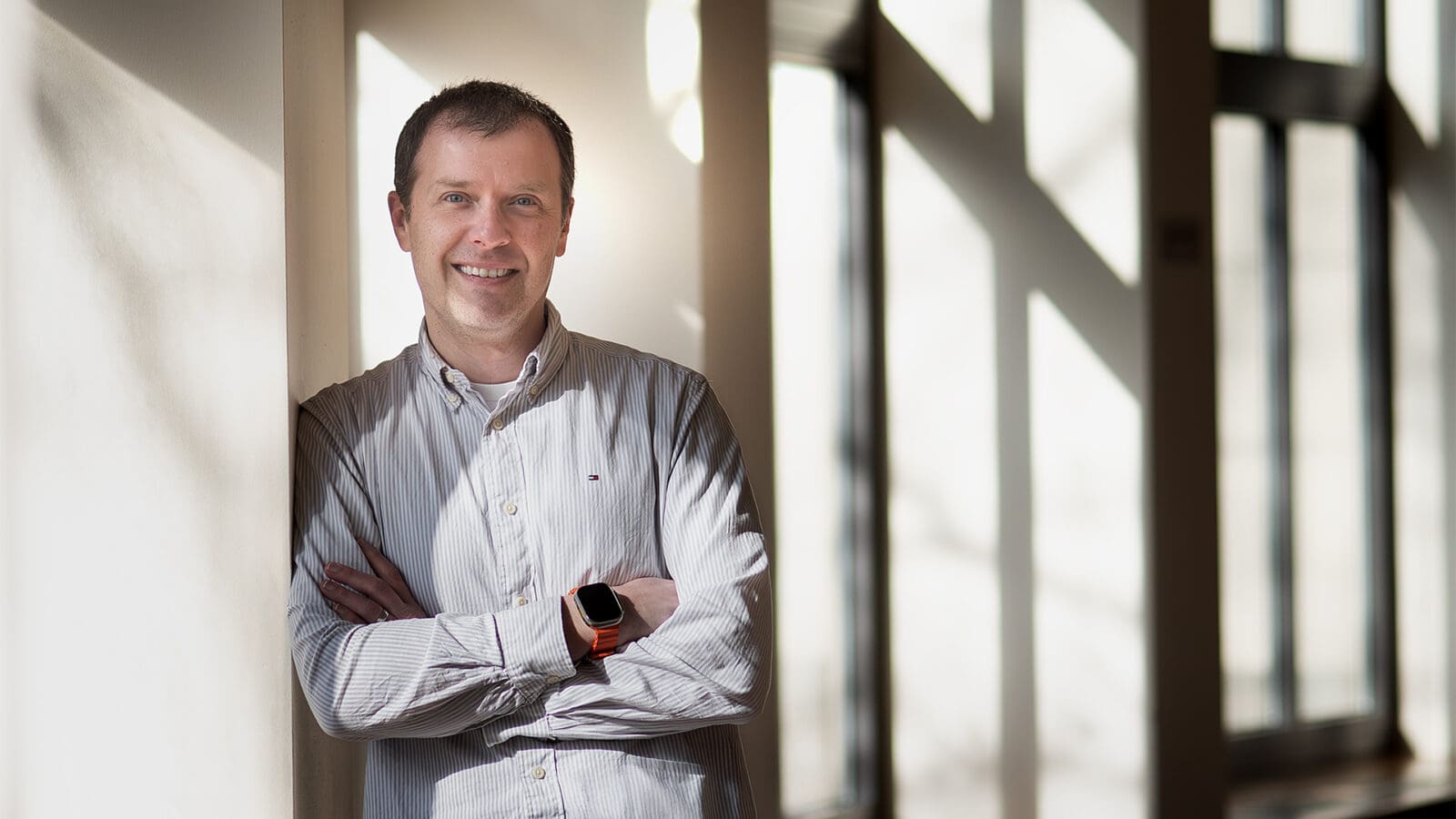 A man stands in a room with large windows