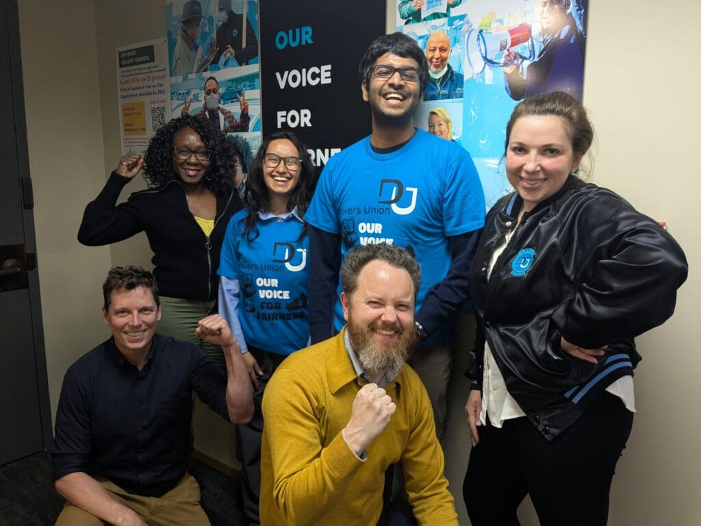 Six people standing in front of a poster, smiling.