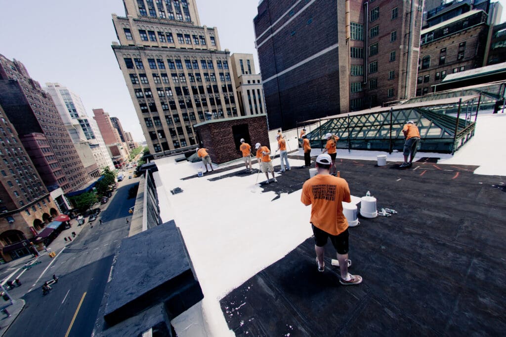 Eight workers on a city rooftop, painting it white.