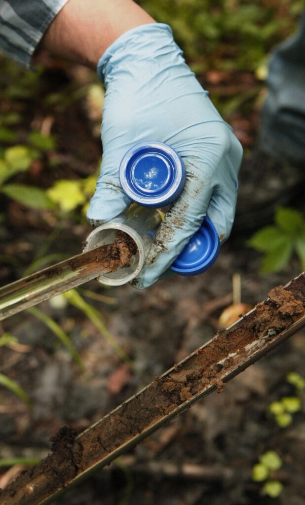 Gloved hands collecting soil samples for testing.