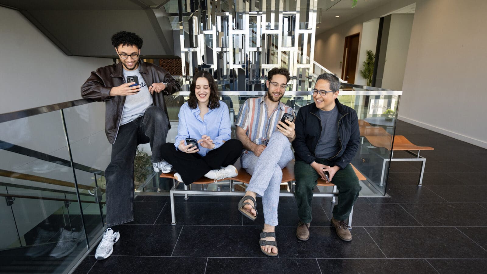 Four researchers sit on a bench together, looking at their phones