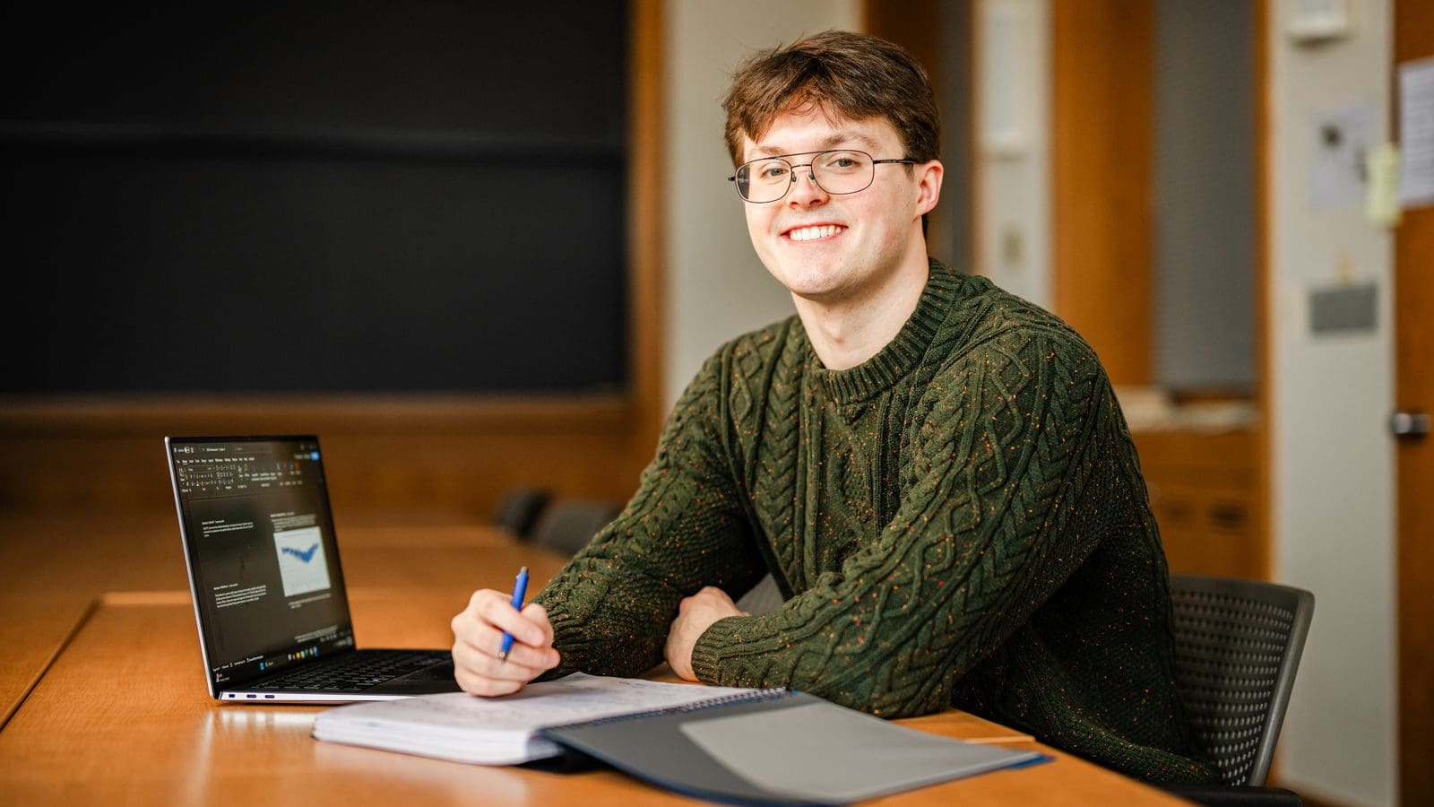 Portrait of Conor McKenna seated at a desk with a laptop and notebook.