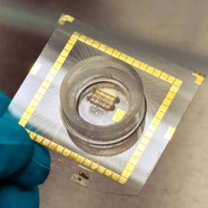 A device featuring gold electrodes surrounding a round reservoir on a clear plastic chip.