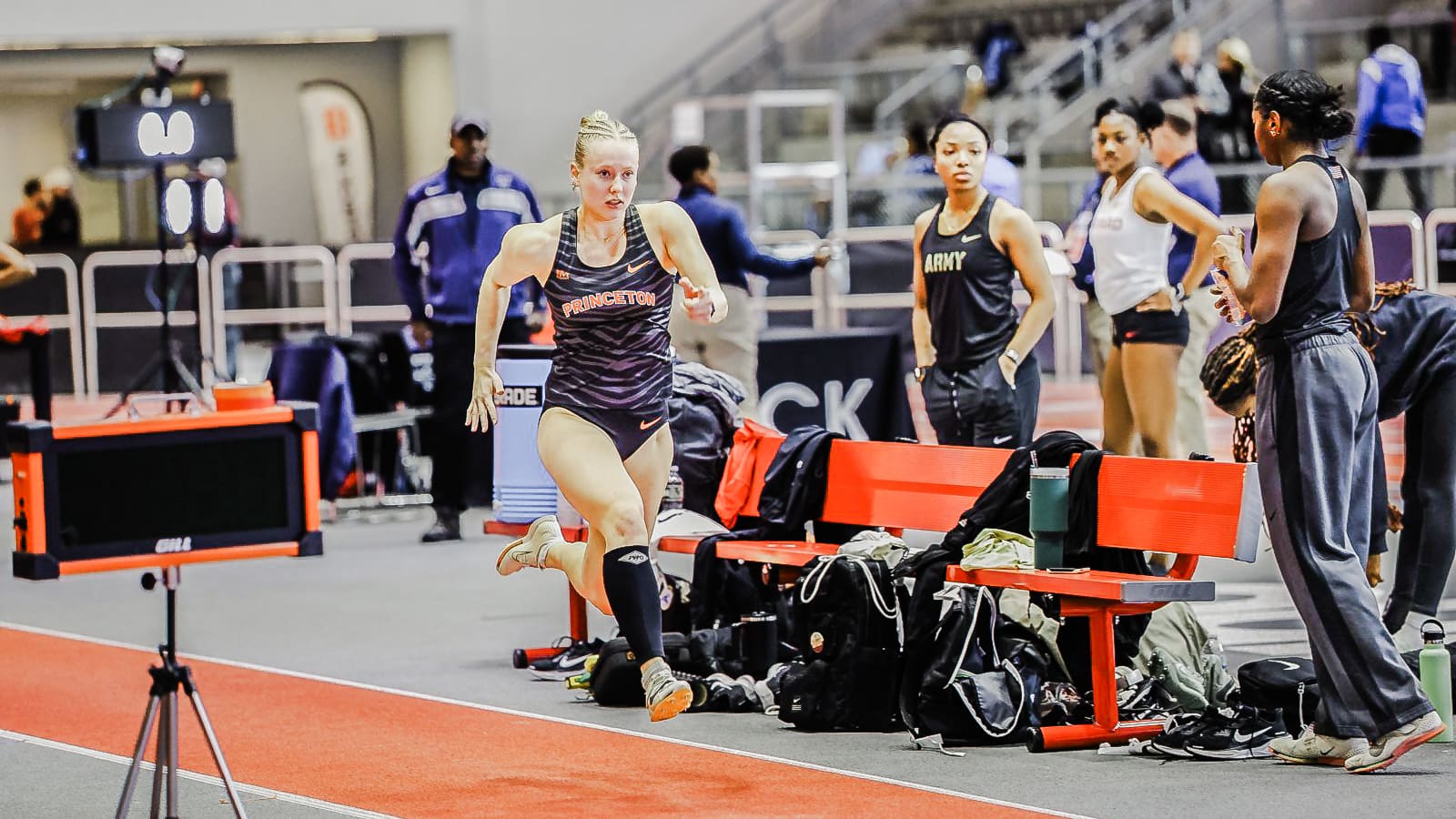 A woman runs on a track while spectators watch from the sidelines.