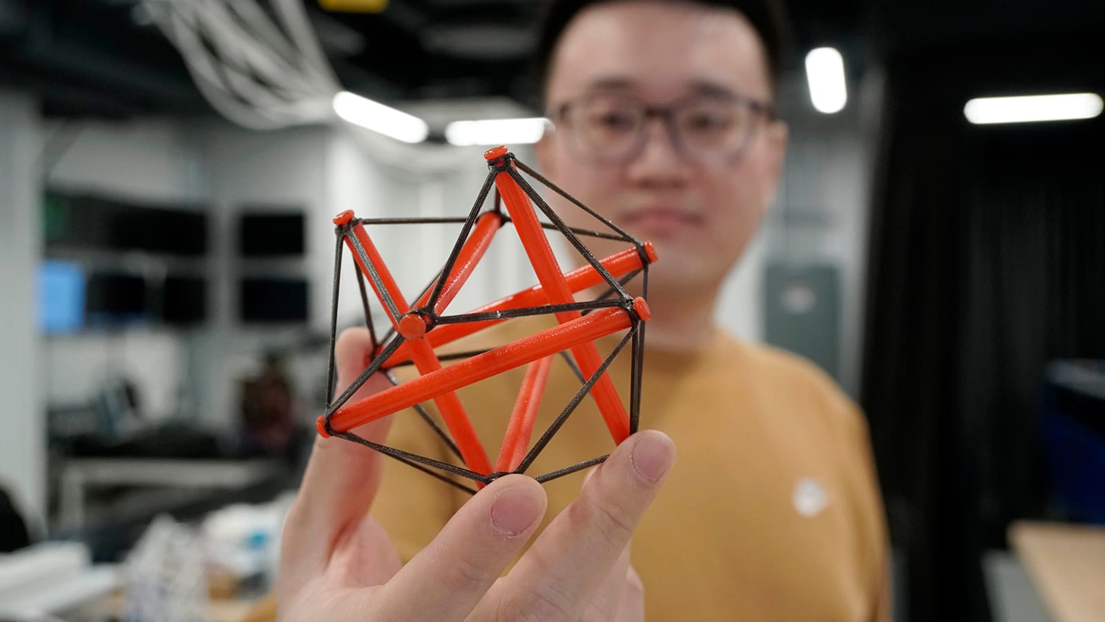 Man presents small figure built of a framework of plastic rods and strings