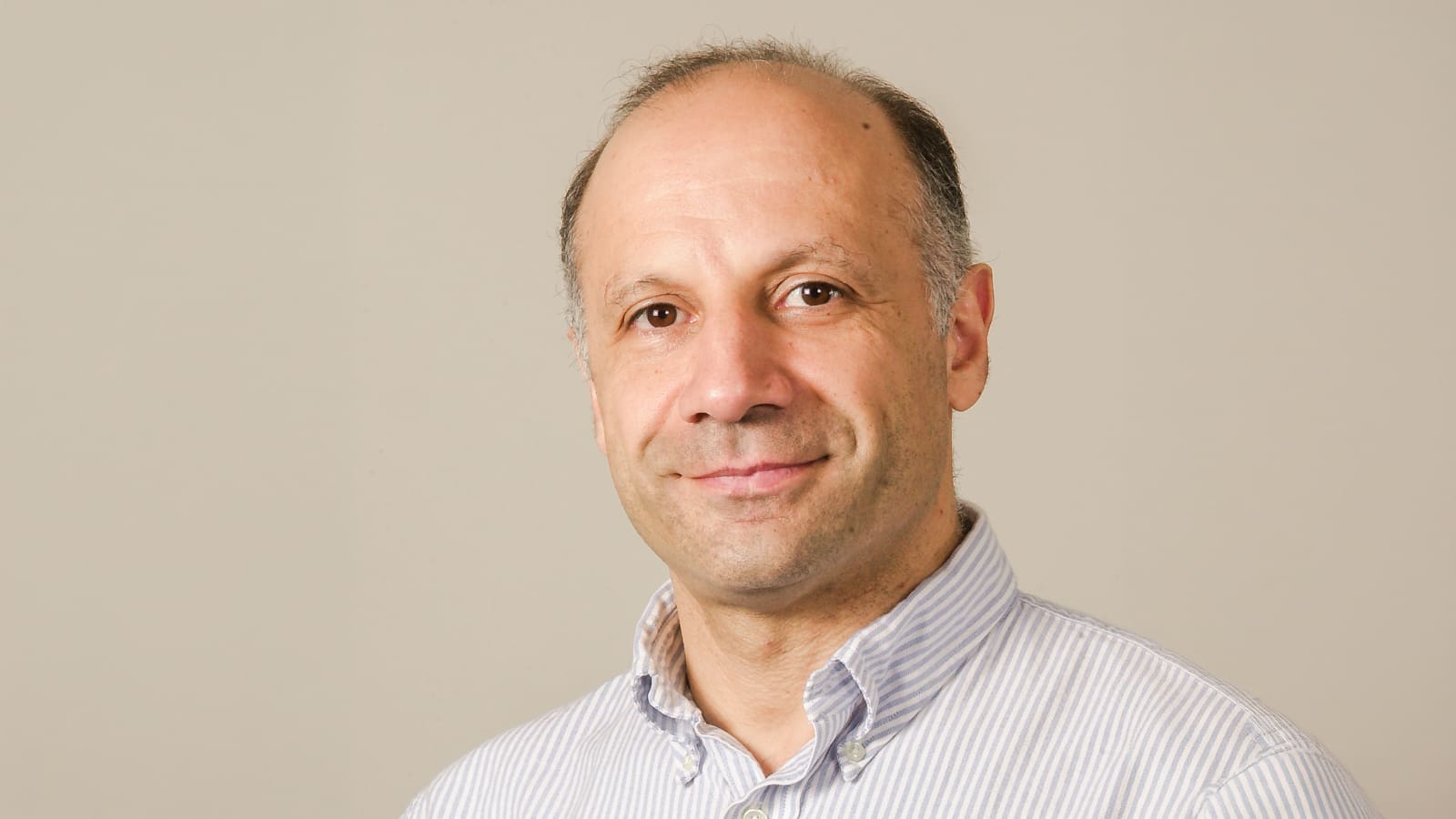 Mansour Shayegan smiling, with beige background.