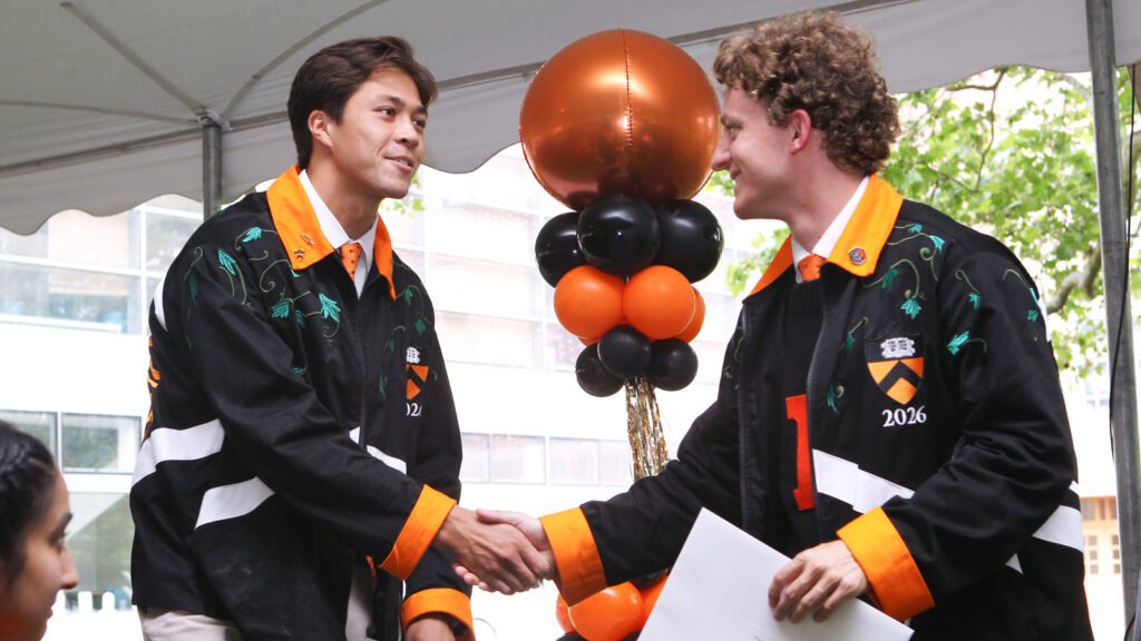 Two men shake hands holding award certificates