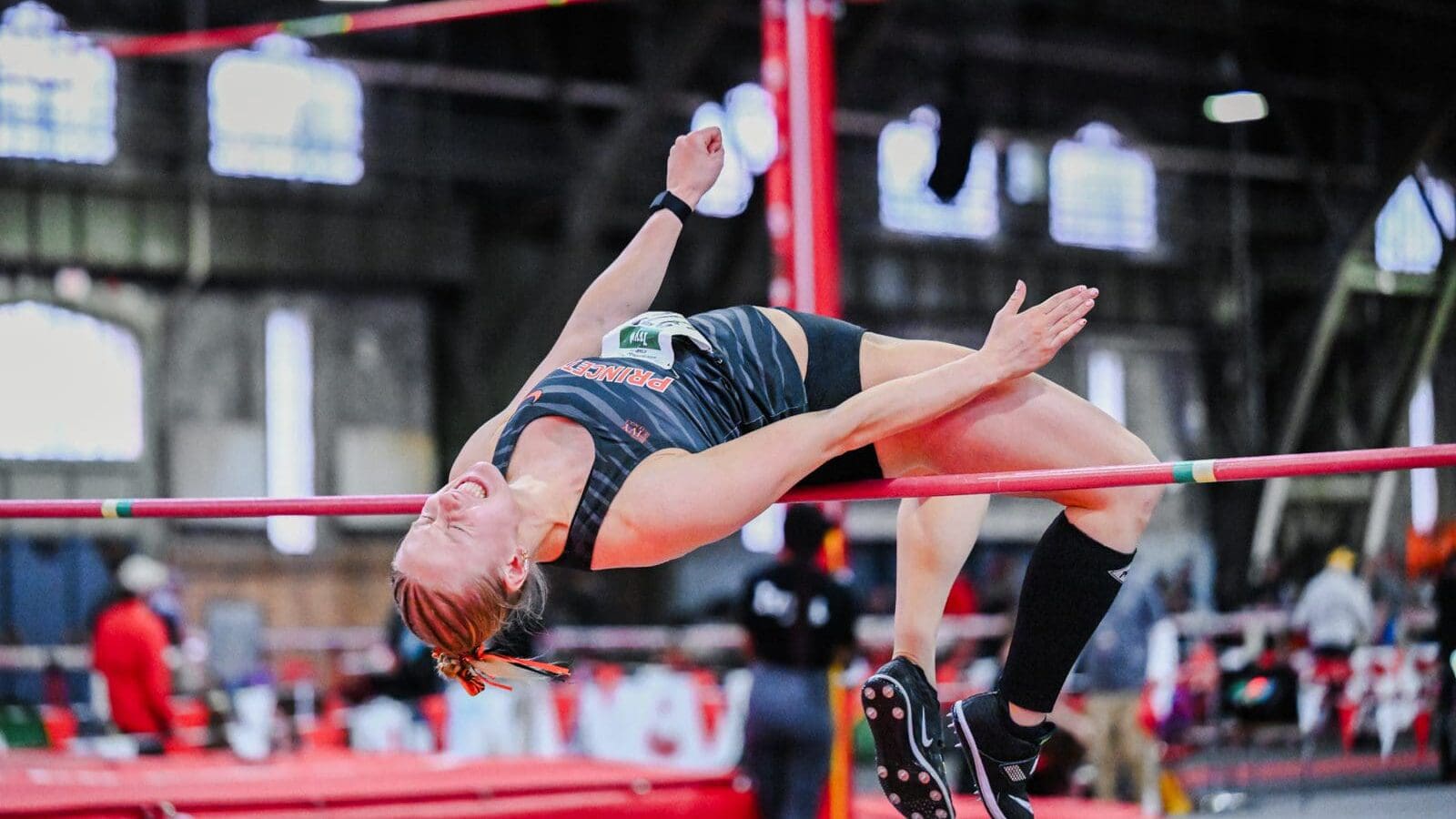 A woman jumping backwards over a bar, her arms extended in front of her.