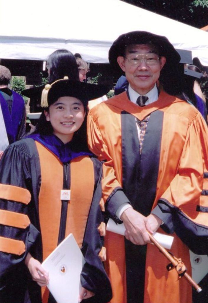 A woman and a man wearing orange and black academic regalia.