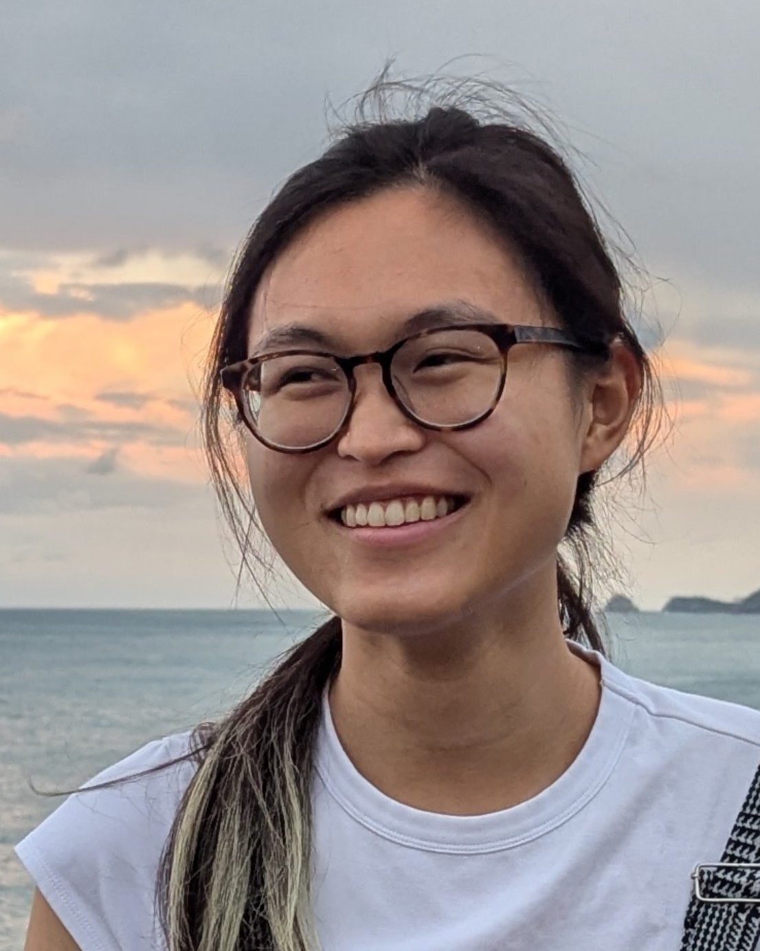 Ewin Tang headshot. She smiling, in front of water and a sunset.