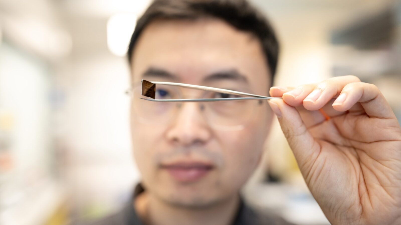 Saien Xie holds up a tiny semiconductor with tweezers