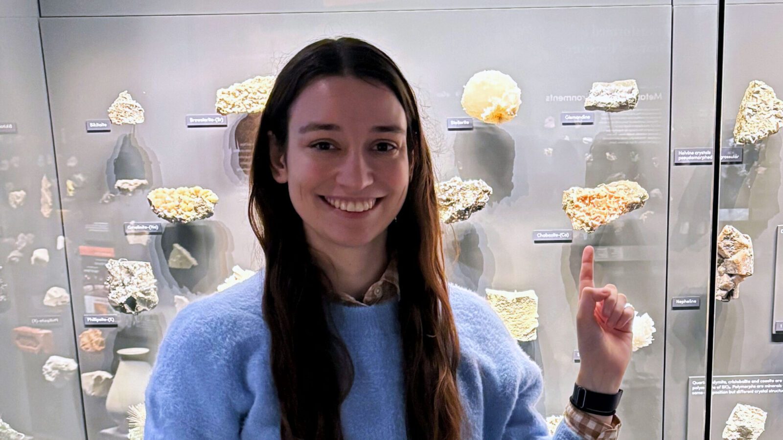 Hannah Snider stands in front of a museum display of zeolite minerals.