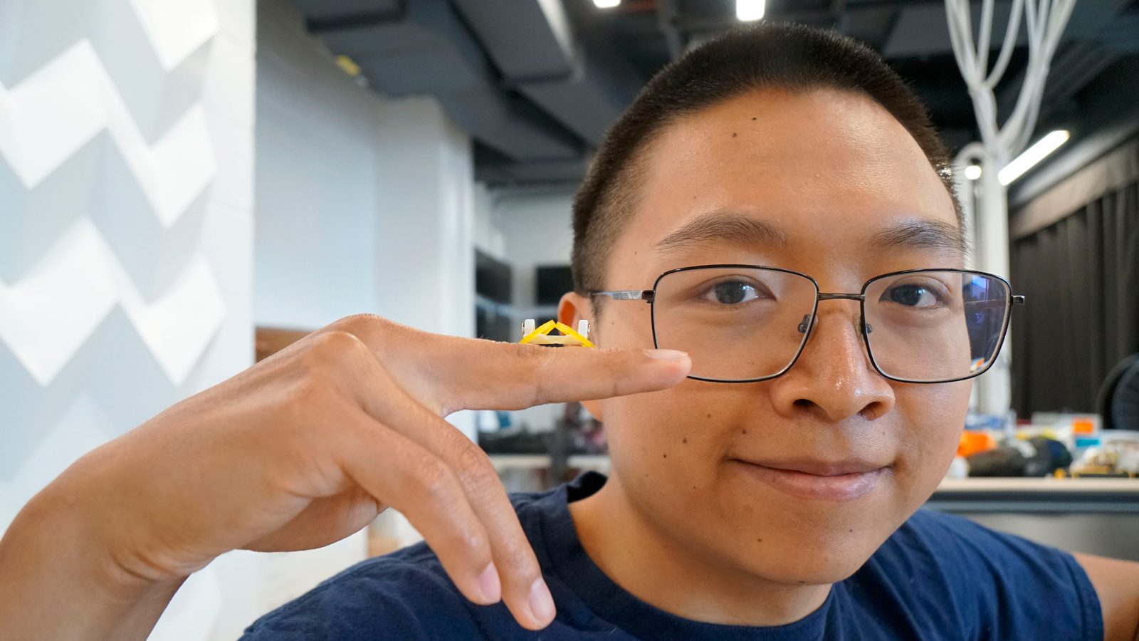 closeup of Princeton researcher's face as he holds a small, plastic yellow robot on his finger.