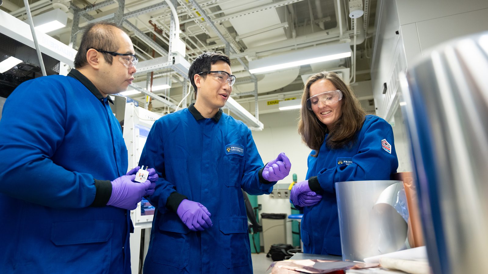 Three researchers in blue lab coats talking in the laboratory
