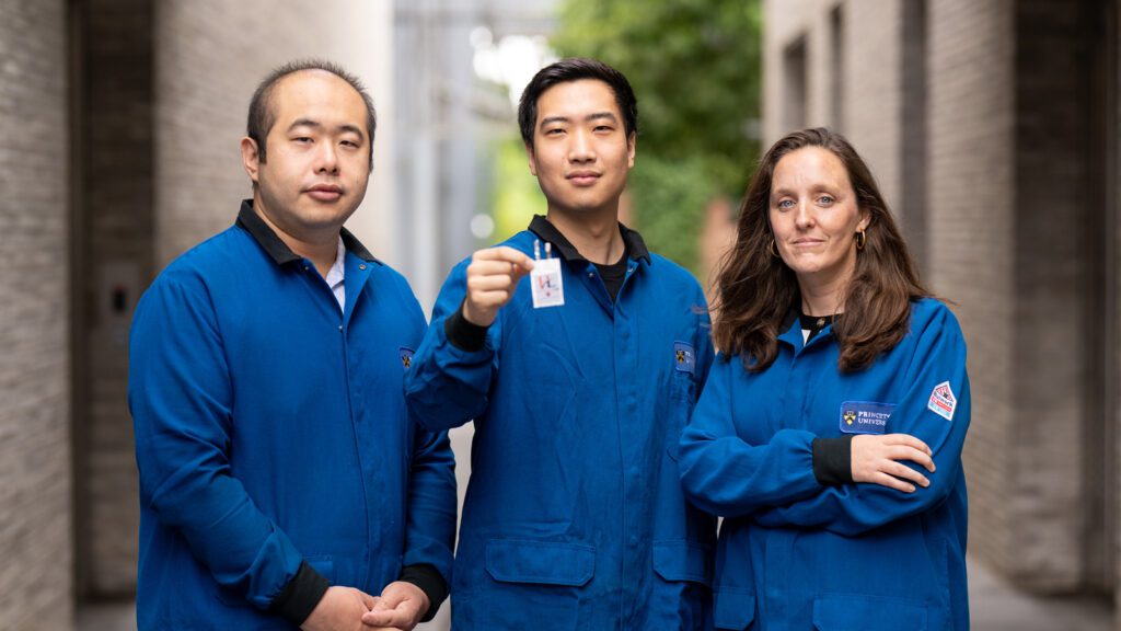 Three researchers stand in a group with the center researcher holding a new battery toward the camera