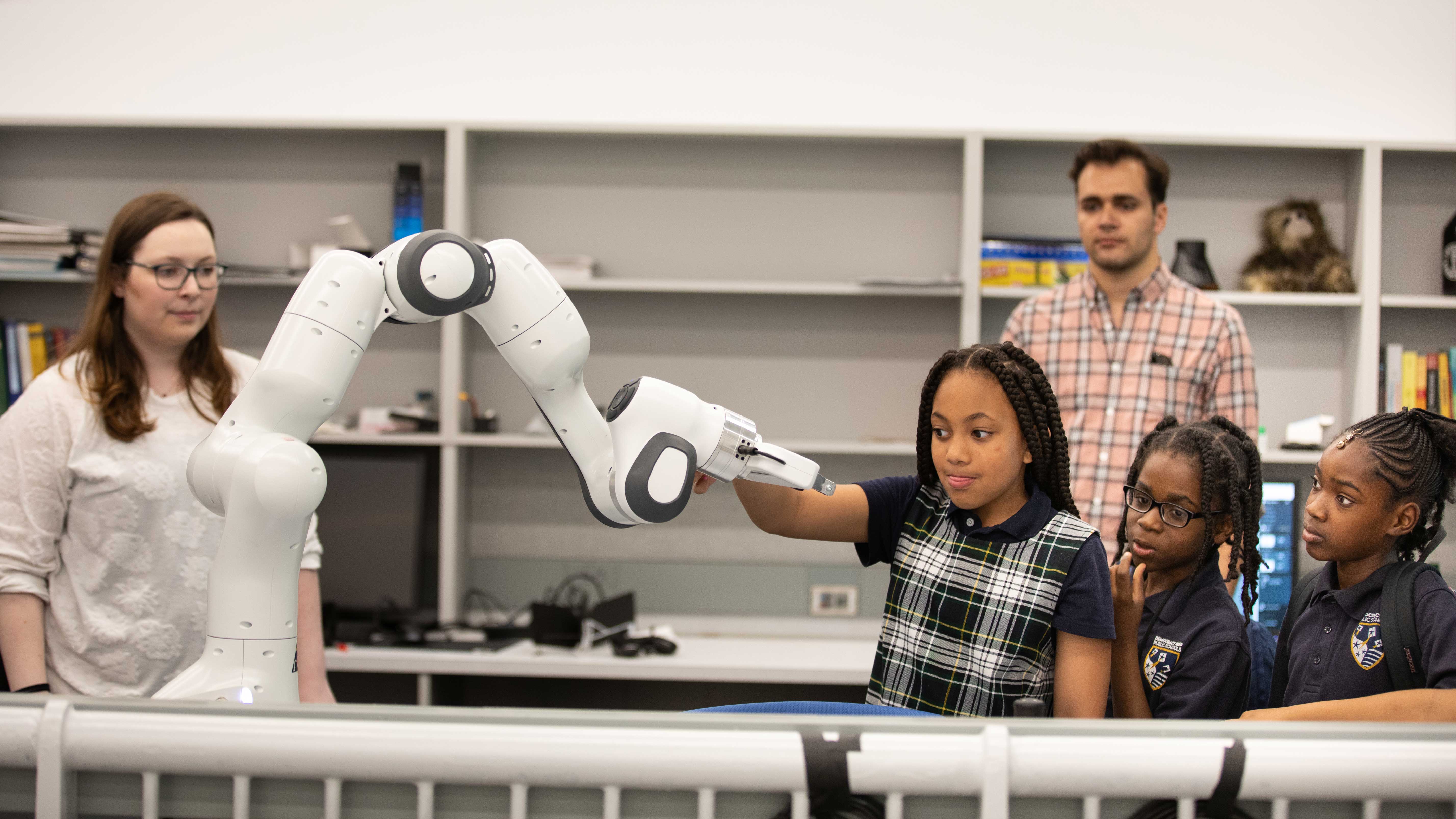 Elementary school students manipulate a robotic arm