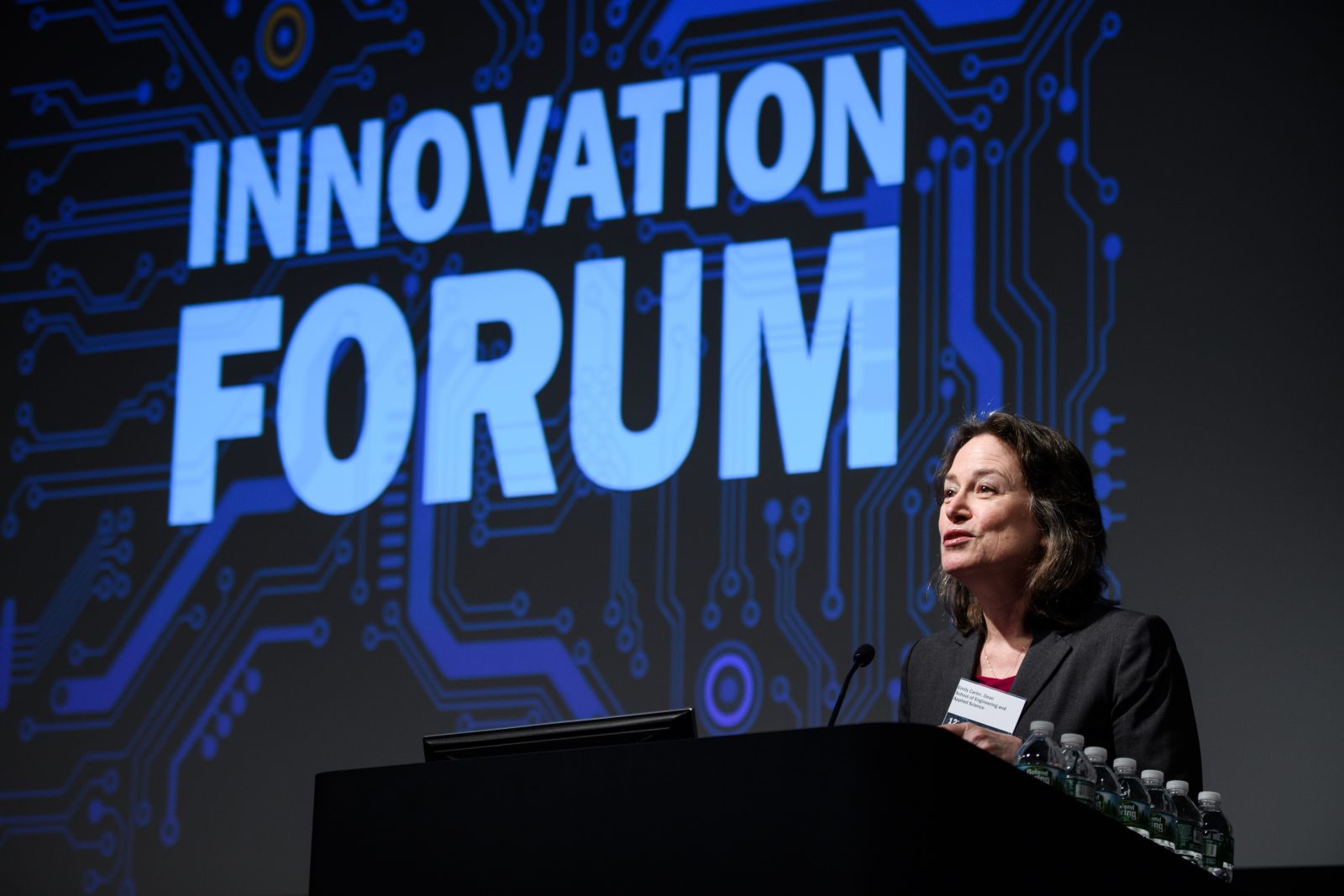 Dean Emily Carter speaks at Innovation Forum, with forum logo projected on the screen