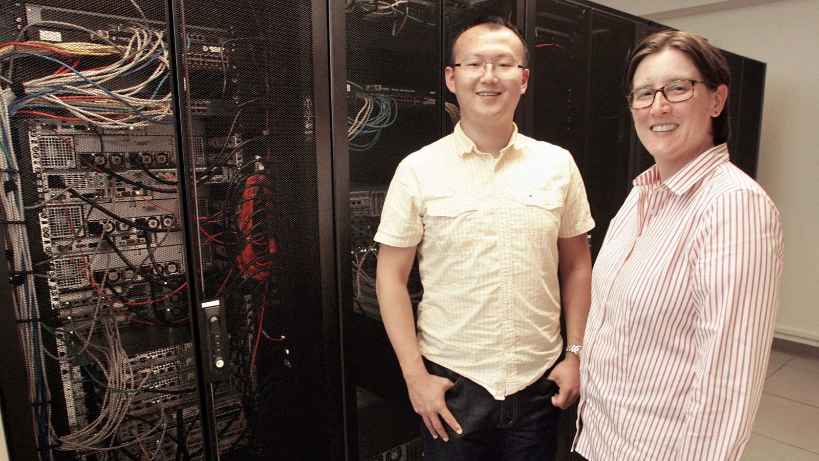 Graduate student and professor stand in front of server rack