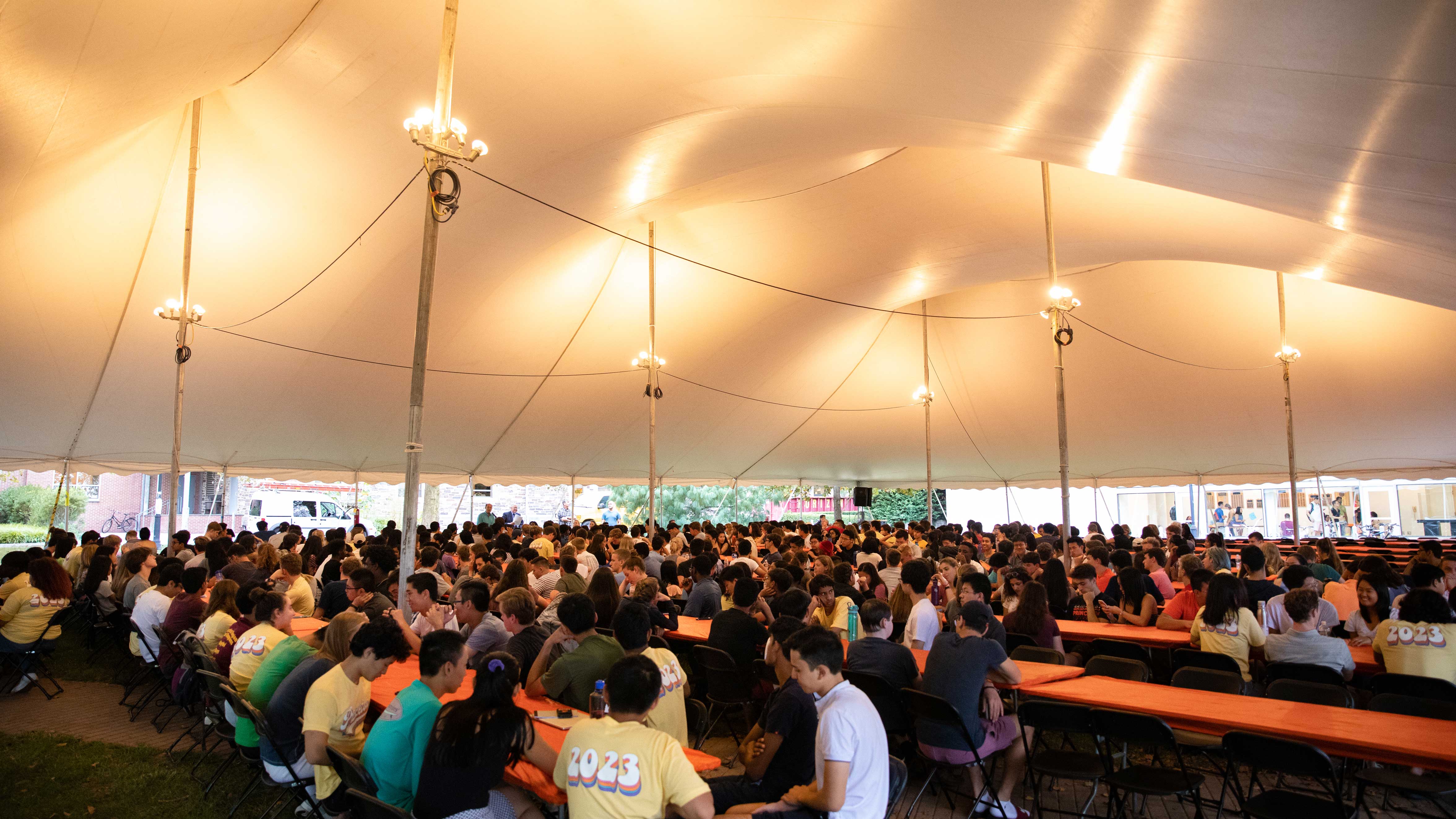 Large group of students sitting at long tables under tent