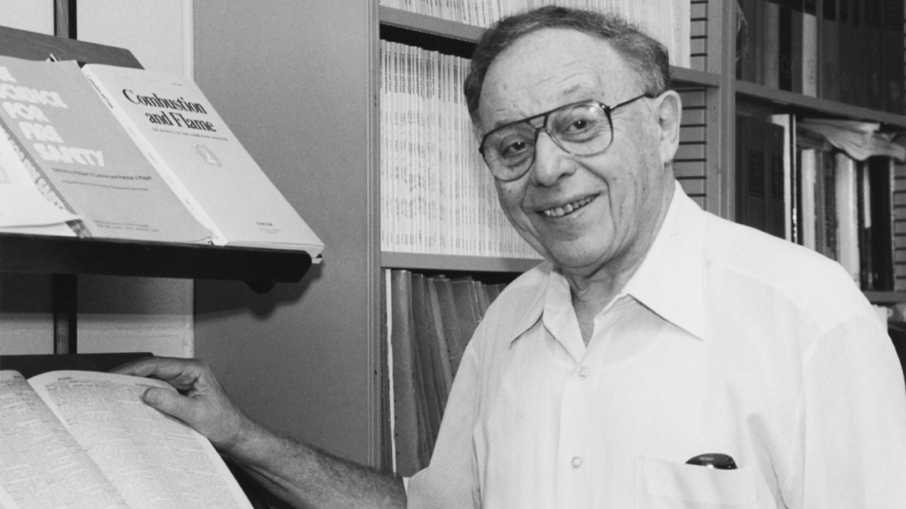 Irvin Glassman black and white photo. He is standing near books and smiling. 