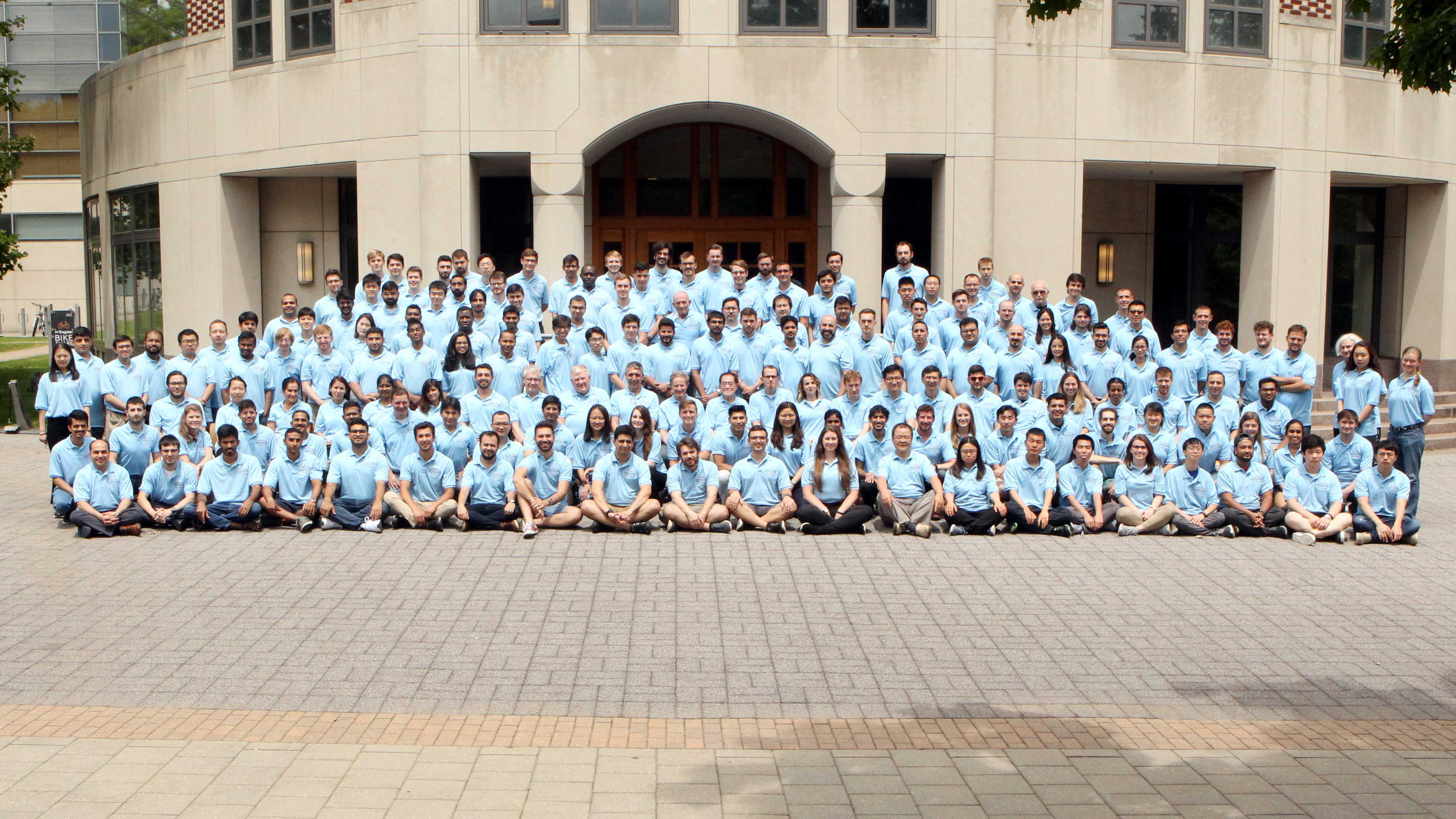 Group of 200 people in light blue shirts posing in front of a building