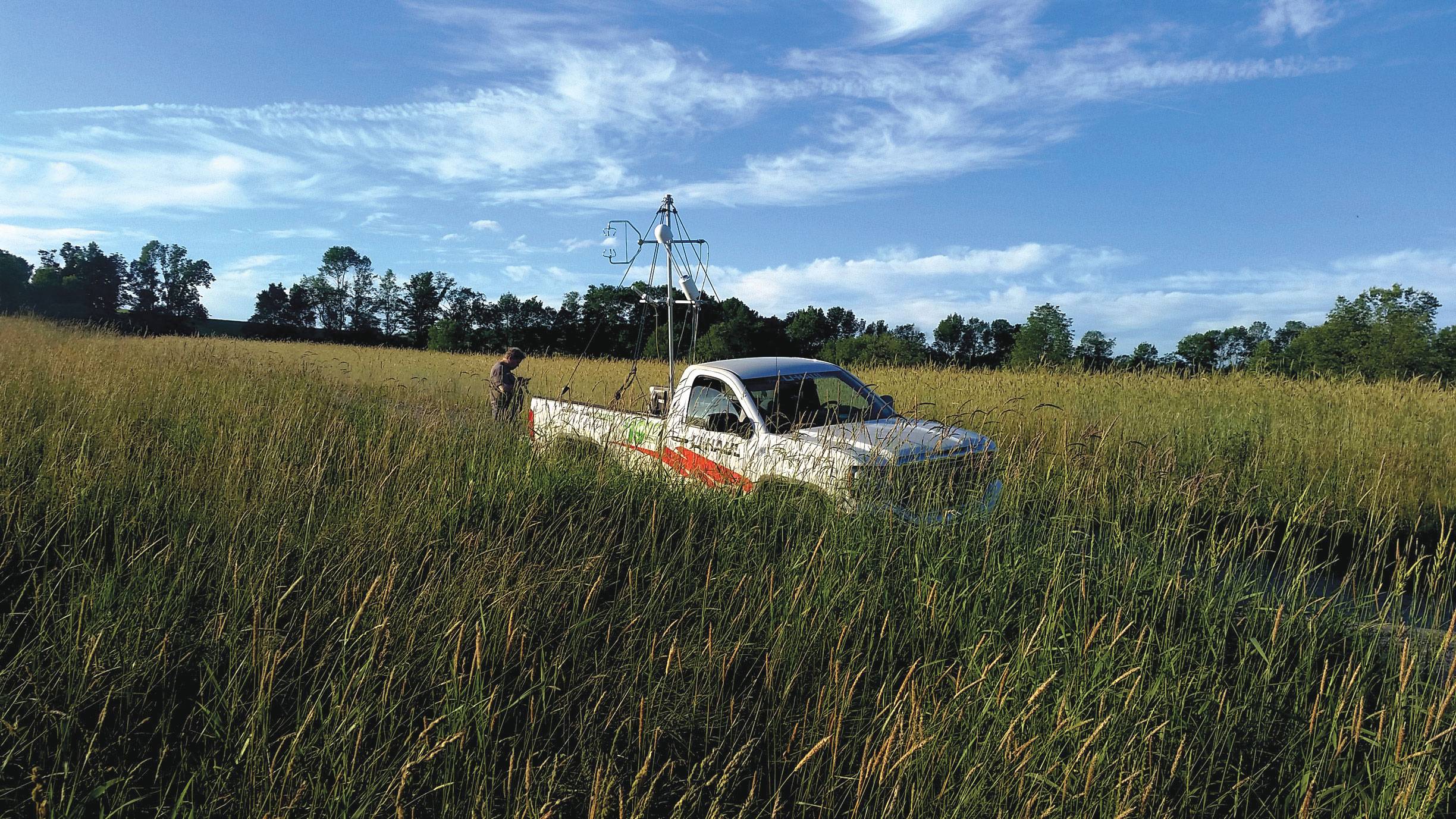 A truck with air pollution measurement equipment in the cab, parked in a tall grassy field.
